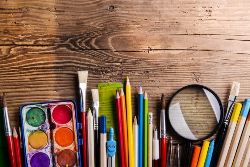 Lápis de cor, lupa e tintas em mesa de madeira