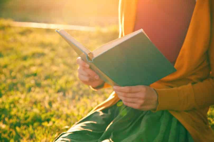 Mãos de mulher segurando livro com sol refletindo