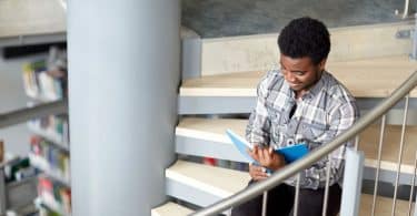 Garoto sentado em escada lendo livro