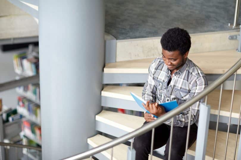 Garoto sentado em escada lendo livro