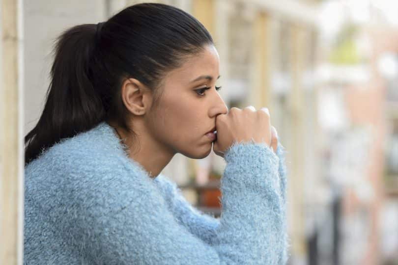 Mulher com expressão triste e cotovelos apoiados com mãos em frente o rosto