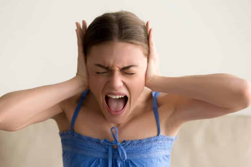Mulher com mãos nos ouvidos e expressão de grito