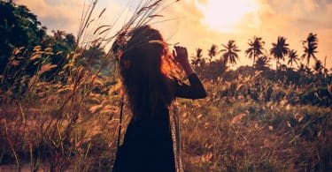 Silhueta de mulher em campo com sol ao fundo