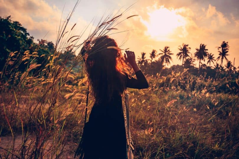 Silhueta de mulher em campo com sol ao fundo