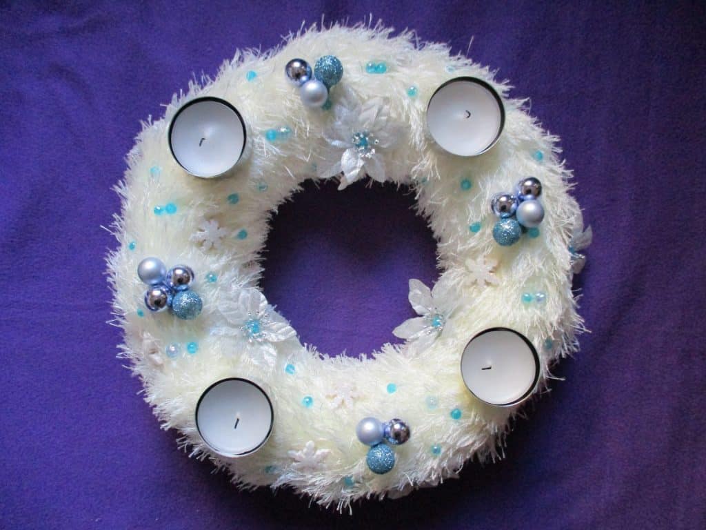 Imagem de uma linda guirlanda de natal na cor branca decorada com velas, flores brancas e azuis e bolinhas azuis e pratas.