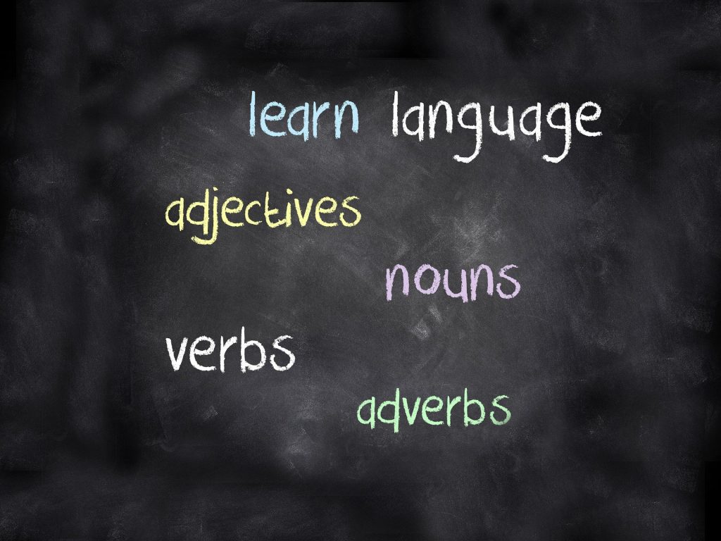 Imagem de um quadro negro com várias palavras escritas em inglês: learn, language, verbs, nouns para serem aprendidas durante uma aula de idiomas.