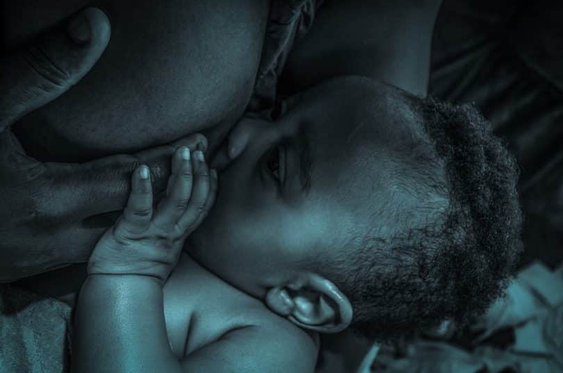 Imagem preto e branco de uma mãe negra amamentando o seu filho.