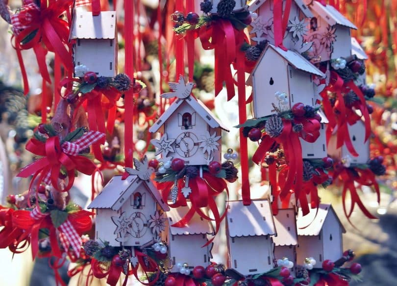 Imagem de várias casinhas de pássaros feita de madeira e pintadas na cor branca e enfeitadas com fitas vermelhas e outros adornos de natal.