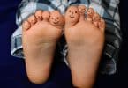 Imagem dos pés de uma criança e os dez dedos estão pintados com uma carinha feliz.
