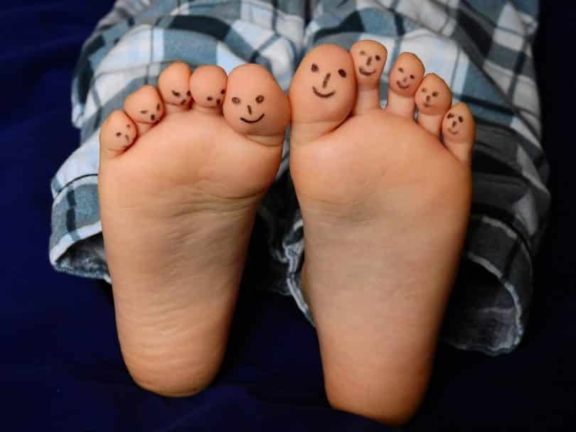 Imagem dos pés de uma criança e os dez dedos estão pintados com uma carinha feliz.