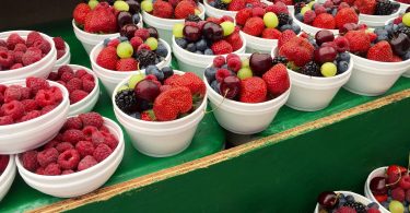 Imagem de vários potes brancos contendo diversos tipos de frutas vermelhas como: morango, uvas mirtilo, que são ricas em antioxidantes.