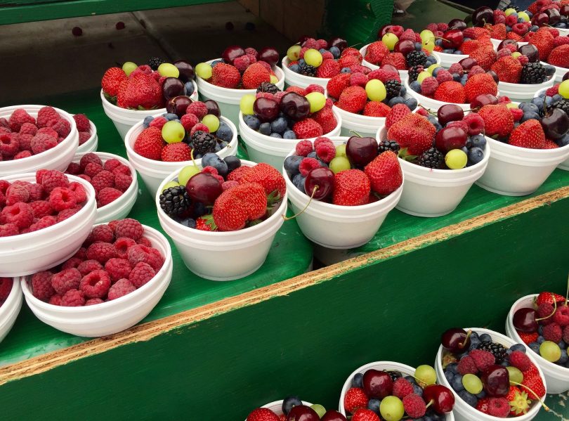 Imagem de vários potes brancos contendo diversos tipos de frutas vermelhas como: morango, uvas mirtilo, que são ricas em antioxidantes.