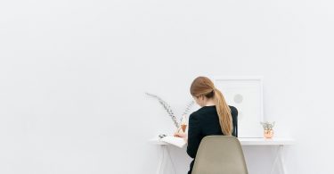 Imagem de uma jovem mulher empreendedora sentada em uma cadeira de frente para uma mesa trabalhando.