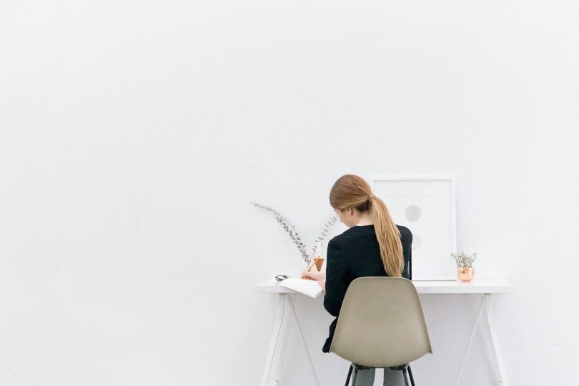 Imagem de uma jovem mulher empreendedora sentada em uma cadeira de frente para uma mesa trabalhando.