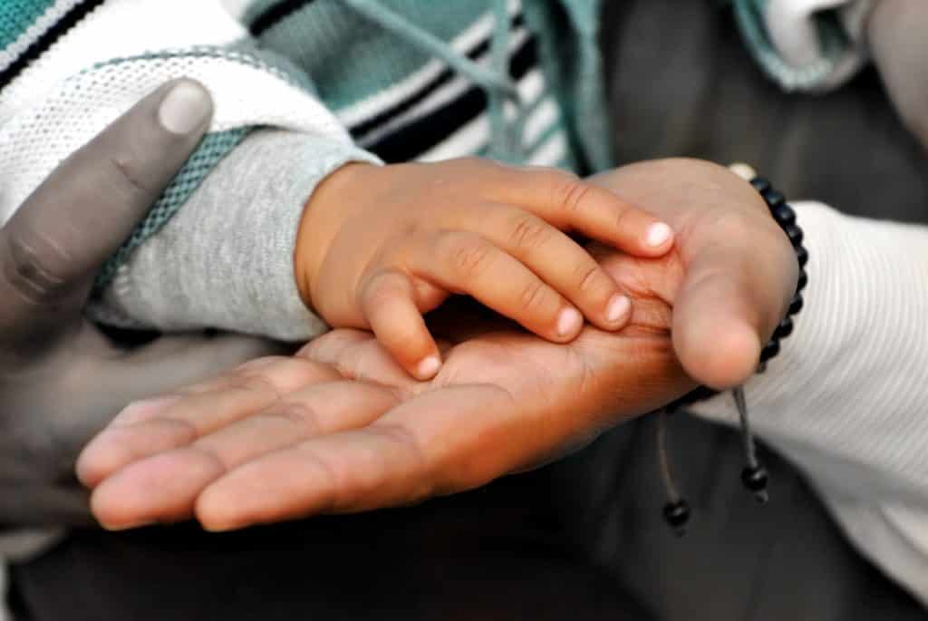 Imagem das mãos de uma pessoa adulta e sobre ela as mãos de uma criança pequena, demonstrando o um gesto de autocuidado de pai com o filho.
