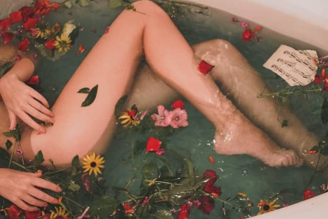 Meio corpo de mulher deitada em banheira com flores espalhadas
