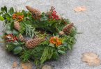 Imagem de uma llinda guirlanda de natal feita na cor verde, decorada com pinhas, flores na cor laranja e vermelho.