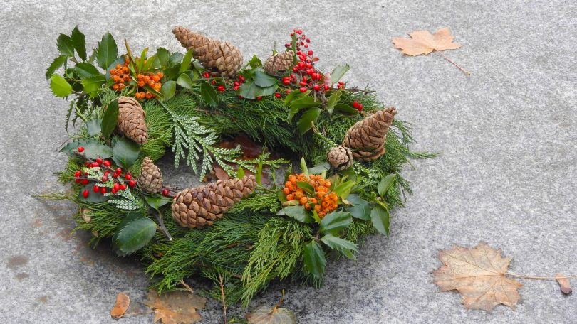 Imagem de uma llinda guirlanda de natal feita na cor verde, decorada com pinhas, flores na cor laranja e vermelho.