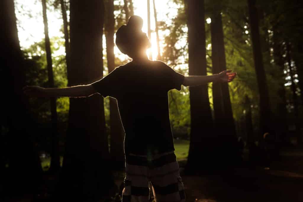 Jovem branco com os braços abertos na floresta.