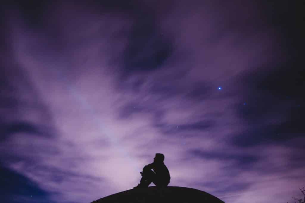 Silhueta de homem sentado com céu roxo ao fundo.