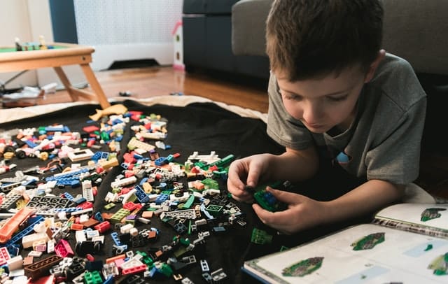 Menino brincando com peças de lego espalhadas no chão