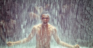 Imagem de um homem negro sorrindo e feliz e ao fundo uma cachoeira.