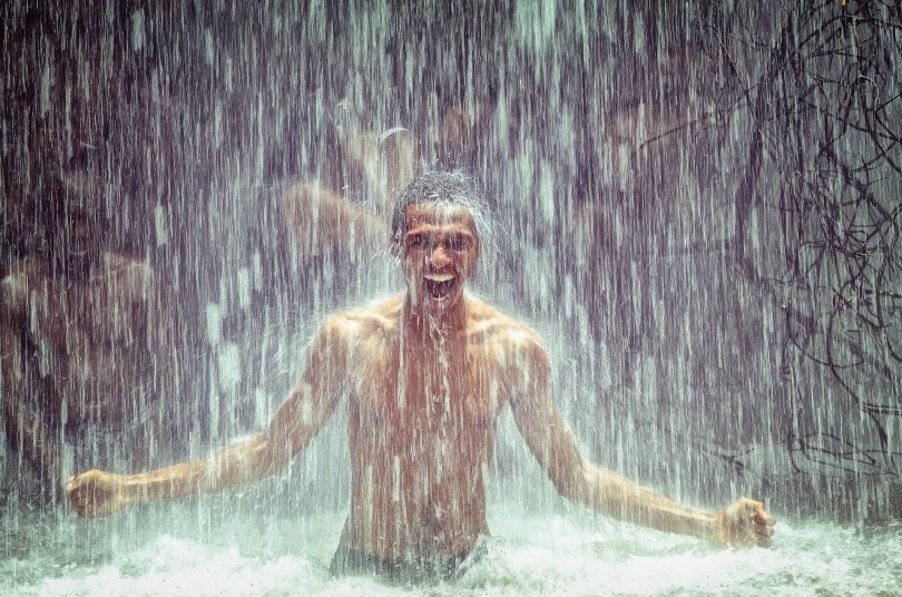 Imagem de um homem negro sorrindo e feliz e ao fundo uma cachoeira.