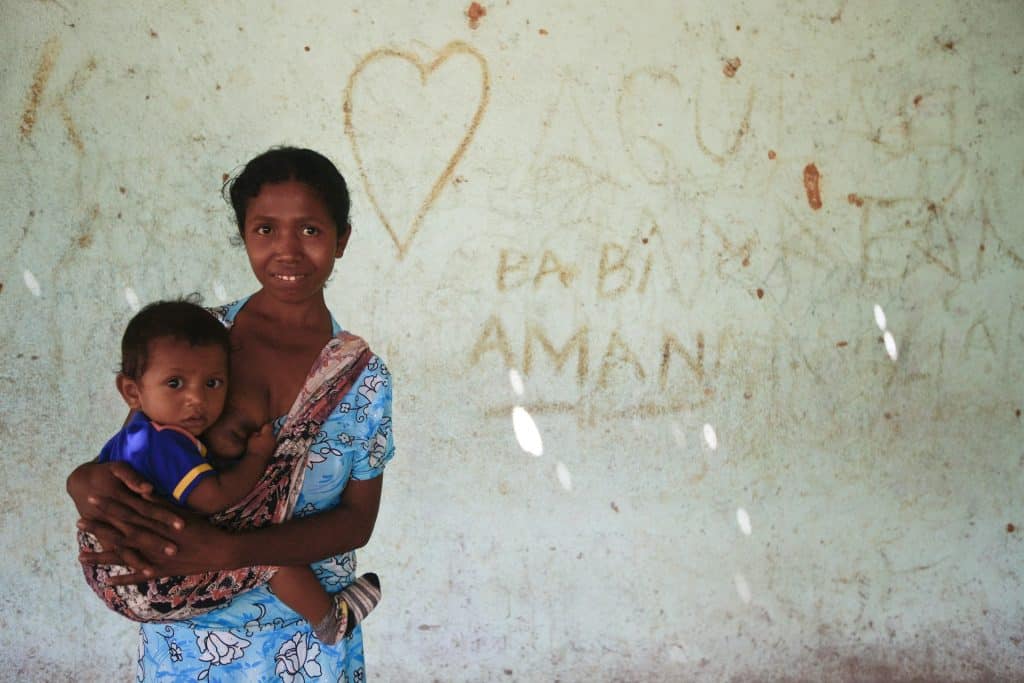 Imagem de uma mulher segurando no colo uma criança. A criança está segurando o seio dela pois acabou de amamentar.