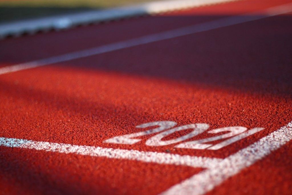 Imagem de uma pista de corrida forrada de vermelho e pintada com faixas brancas nas laterais. Nela está escrito a palavra 2021 em letras grandes na cor branca.