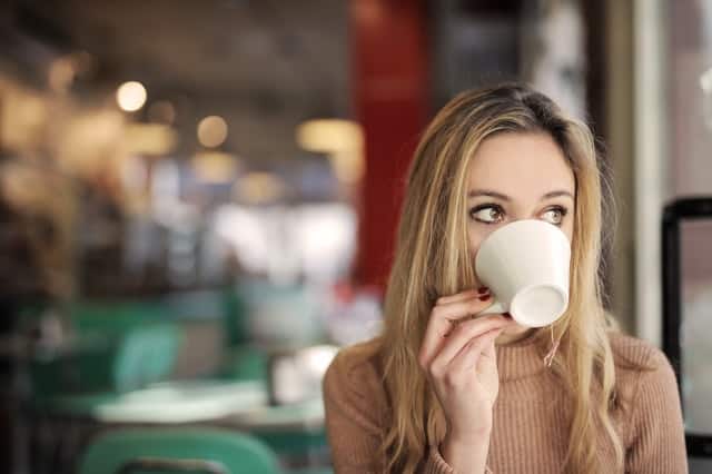 Mulher virando xícara de café na boca