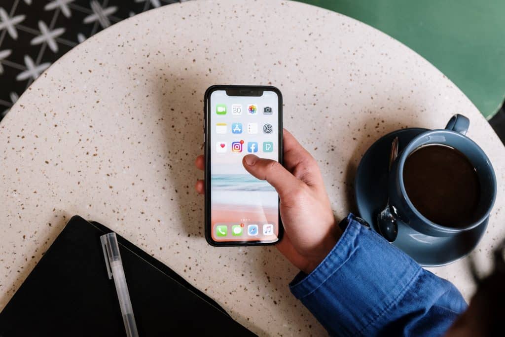 Pessoa segurando celular com aplicativos ao lado de uma xícara de café