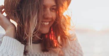 Mulher segurando chapéu e sorrindo