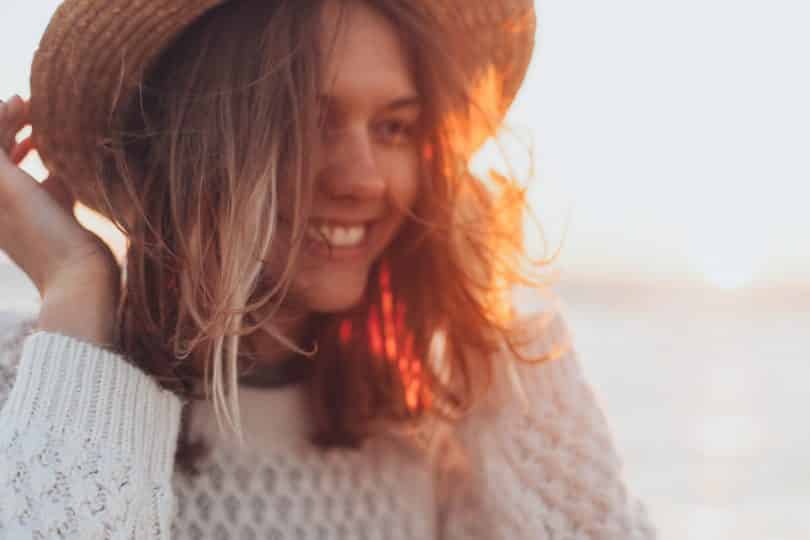 Mulher segurando chapéu e sorrindo