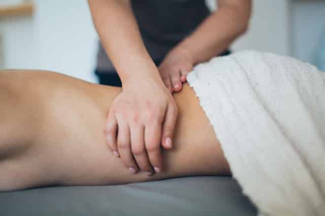 Par de mãos brancas femininas realizando massagem em corpo feminino branco.