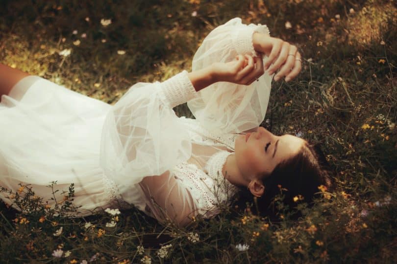 Mulher deitada em um gramado olhando para suas mãos