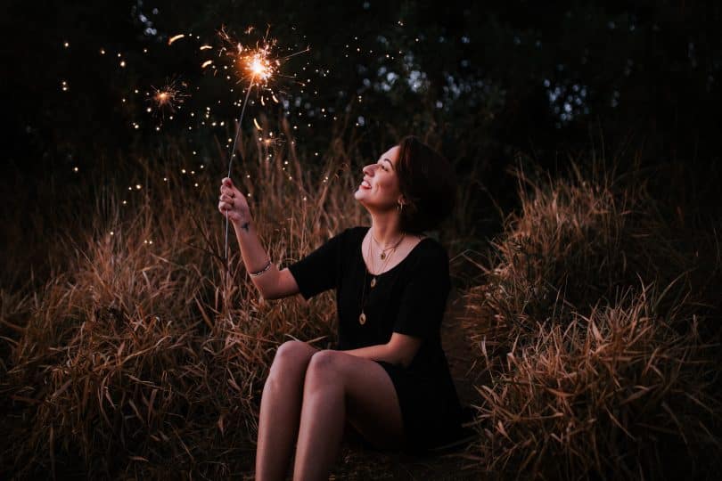 Mulher sentada em um gramado sorrindo segurando uma vela