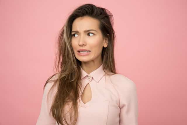 Mulher com expressão tensa em pé vista de frente em fundo rosa