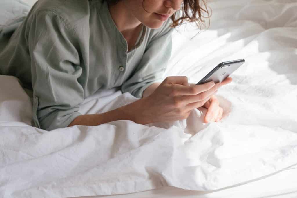 Mulher deitada na cama usando celular