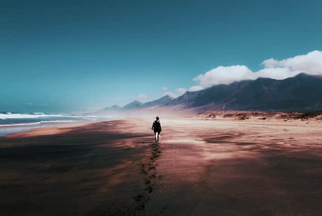 Pessoa caminhando em praia com montanha céu e nuvens ao fundo