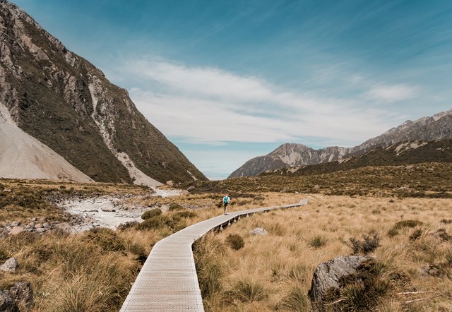 Homem andando em ponte no deserto com montanhas ao fundo