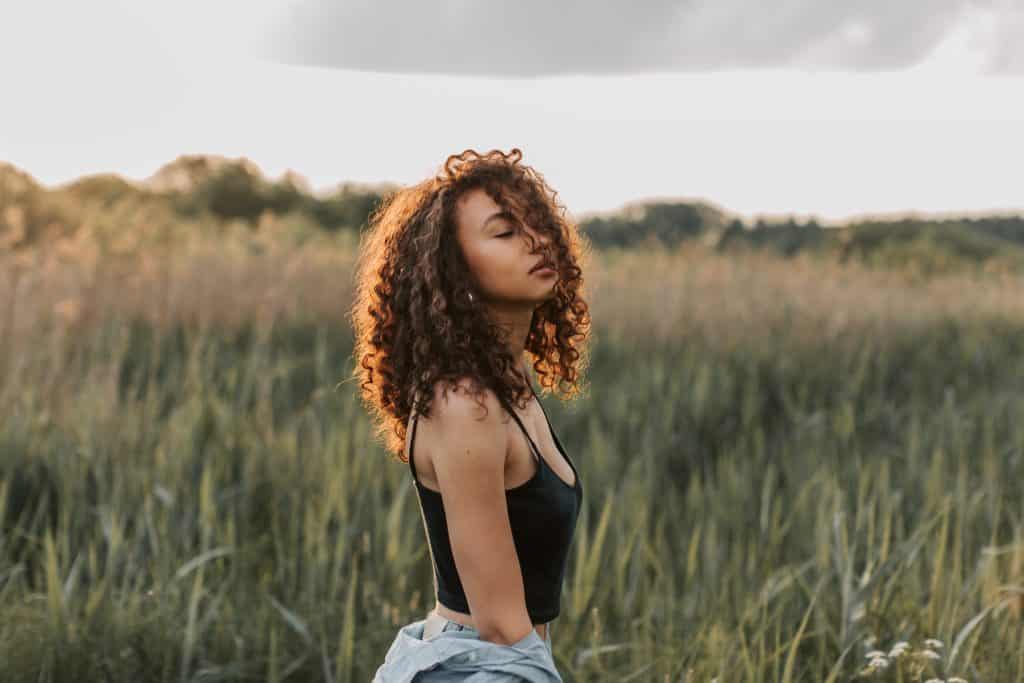 Mulher em um campo de gramado de olhos fechados e cabelo no rosto