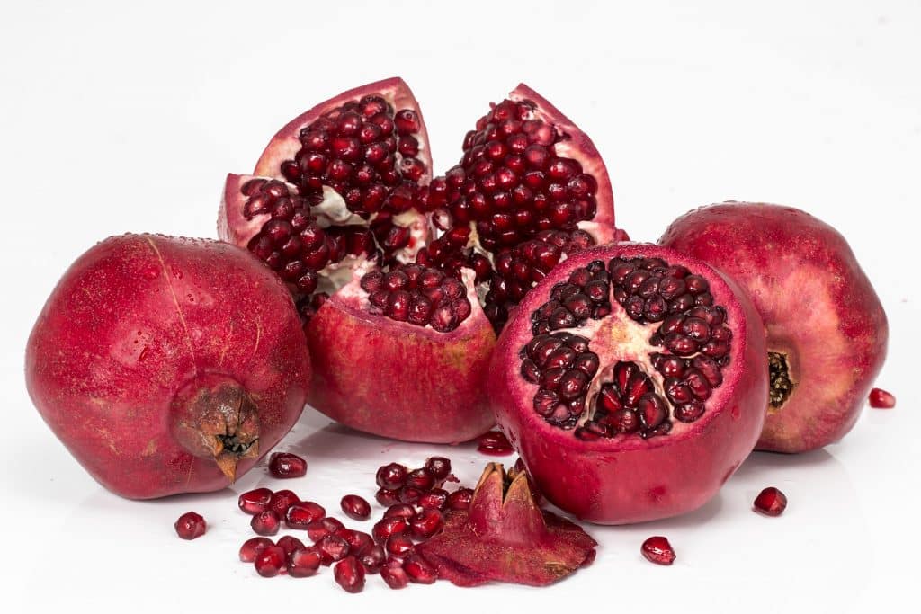 Imagem da fruta romã, algumas estão inteiras e as outras cortas ao meio mostrando as suas sementes. A fruta é muito rica em antioxidantes.