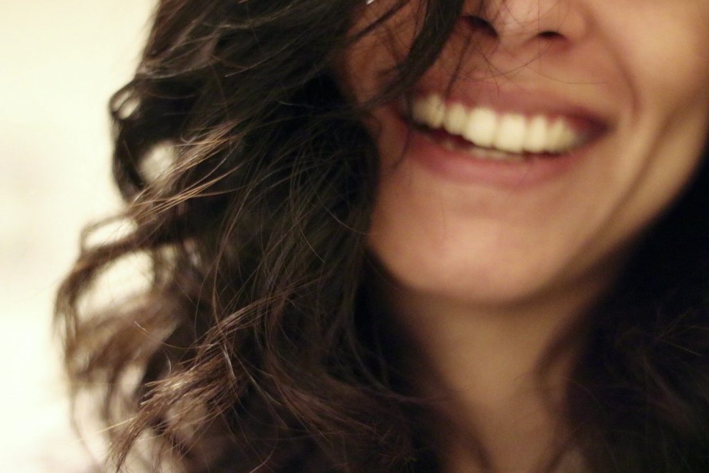 Imagem de um lindo sorriso de uma mulher de cabelos escuros, longos e ondulados.