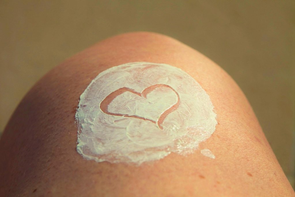 Imagem da perna de uma pessoa e sobre ela está espalhado um pouco de protetor solar desenhado com o formato de um coração.
