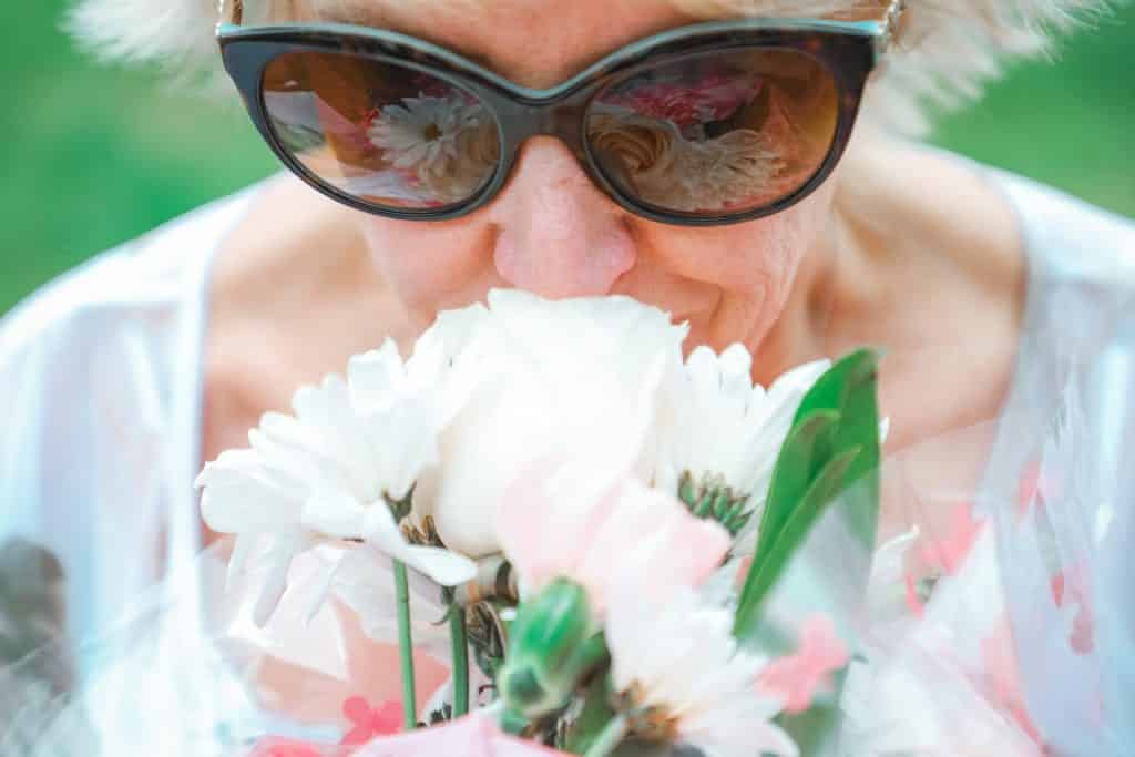 Idosa branca cheirando buquê de flores.