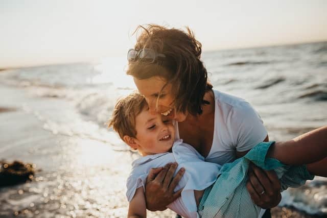 Mãe com filho nos braços com mar ao fundo