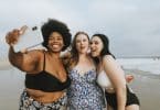 Duas mulheres brancas e uma negra de biquíni na praia.
