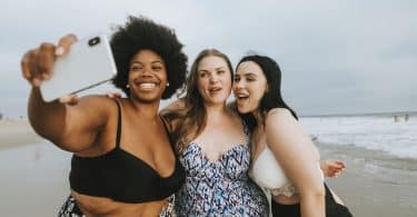 Duas mulheres brancas e uma negra de biquíni na praia.