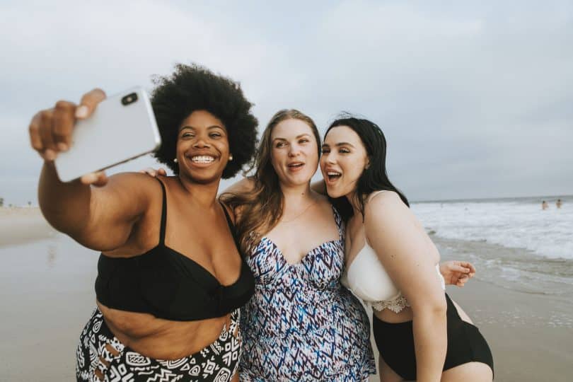 Duas mulheres brancas e uma negra de biquíni na praia.