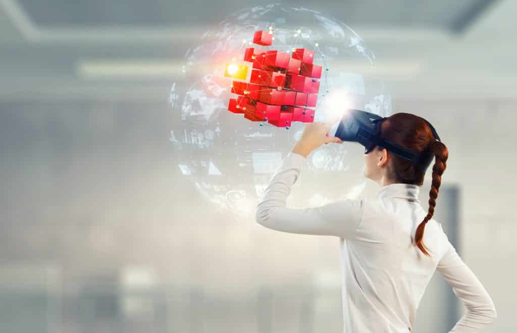 Imagem de uma jovem mulher usando um óculos 3D. Ela está olhando para um cubo vermelho centralizado dentro de uma bolha transparente.